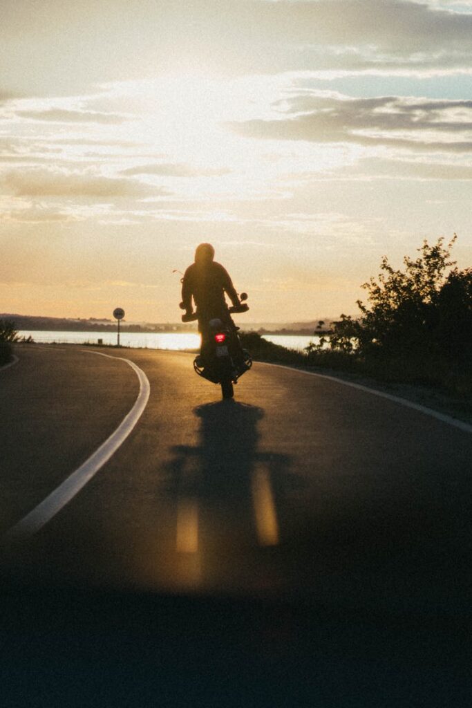 Silhouette of a motorcyclist riding on a scenic road during a beautiful sunset, emphasizing freedom and adventure.